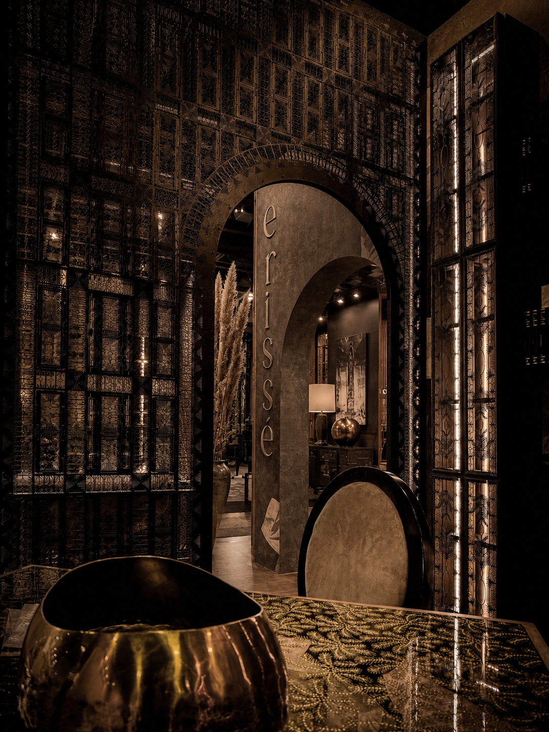 Moody interior design featuring dark metal embroidery wall and a glass table featuring gold leaf inserts
